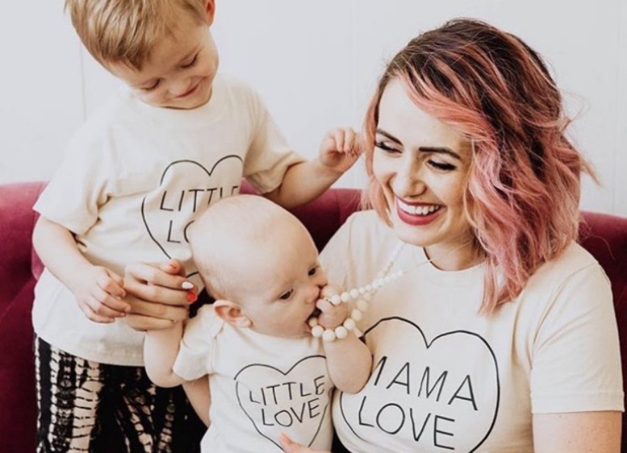 Woman wearing cream colored silicone teething necklace while baby is chewing on it